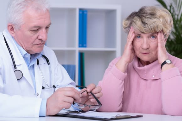 A frustrated senior woman with her hands on her head having a discussion with a doctor.