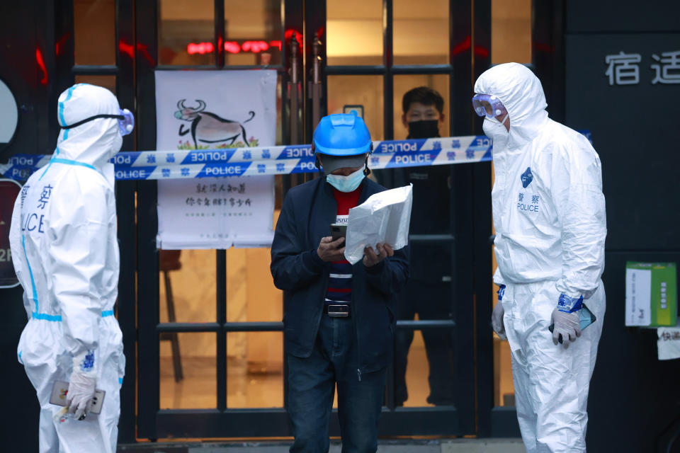 A delivery man walks by police officers with protective suit outside of a hotel in Shanghai, China, Tuesday, Mar. 15th, 2022. China's new COVID-19 cases Tuesday more than doubled from the previous day as the country faces by far its biggest outbreak since the early days of the pandemic. (AP Photo)