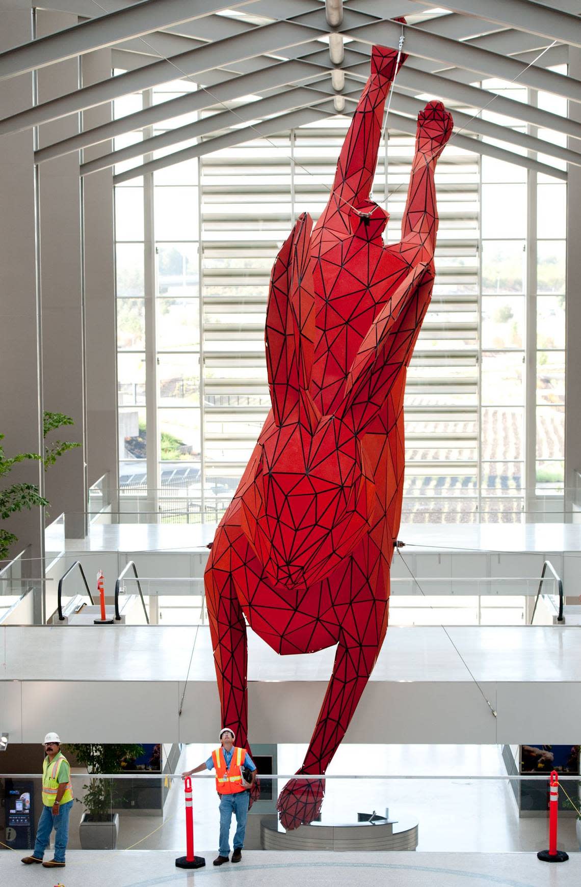 Construction workers mingle around the 56-foot-long, 15-foot diameter “Leap”, a red rabbit made of steel and aluminum by Denver artist Lawrence Argent, as it hangs from cables inside Terminal B at Sacramento international Airport on Friday, Sept. 9, 2011.