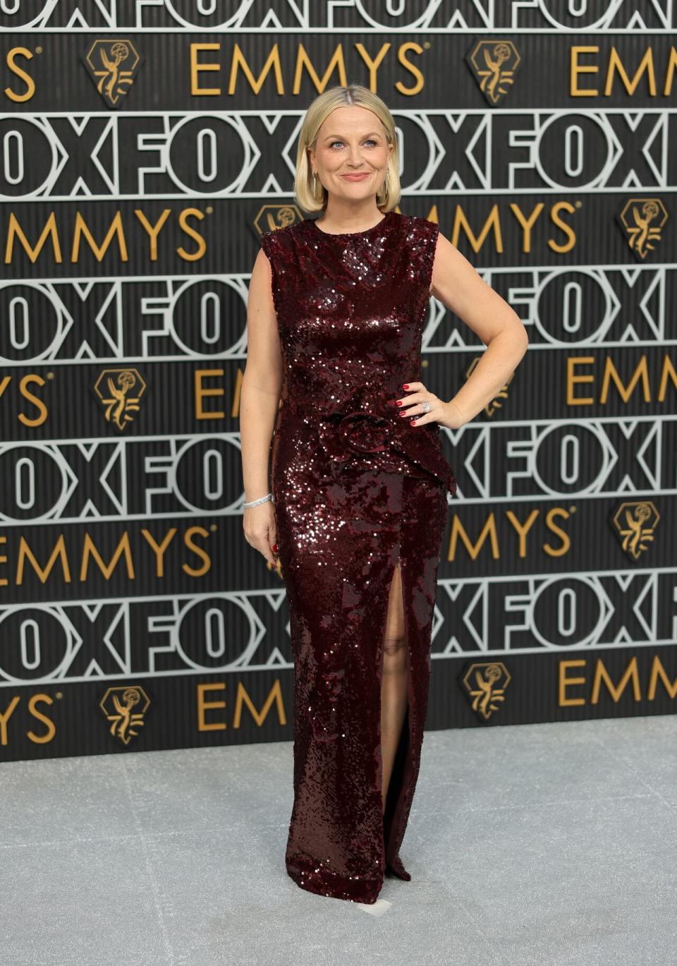 Former Parks and Recreation star Amy Poehler wears a wine-coloured short sleeve dress with a high slit in the leg. 