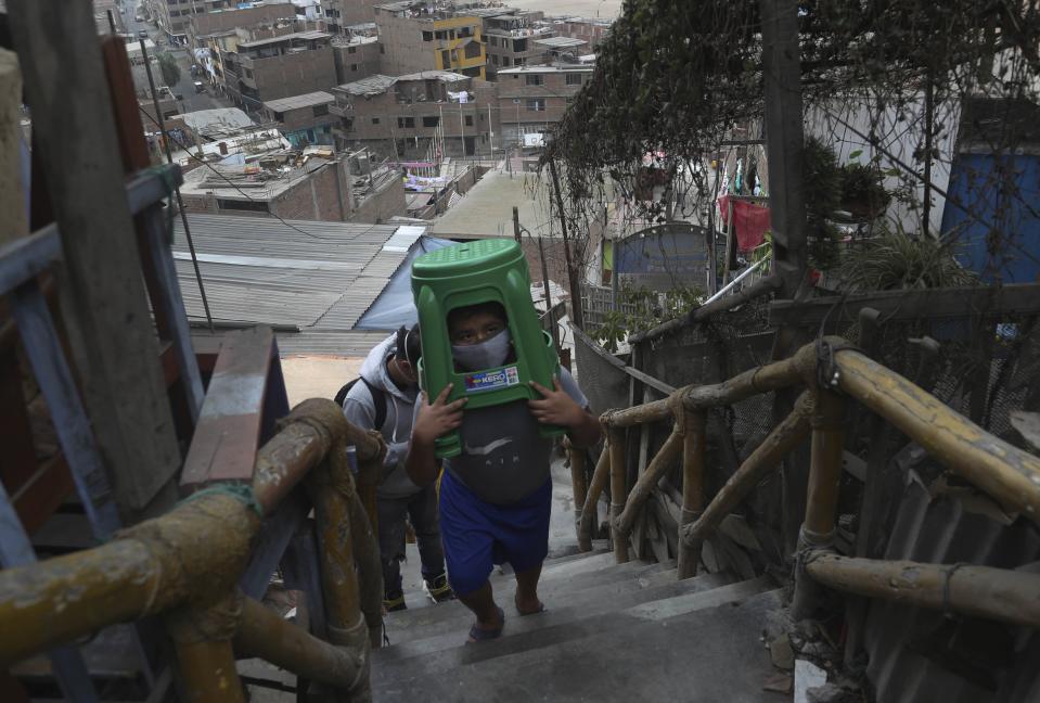 Twelve-year-old Yacdel Flores, hauling hard plastic stools, ascends a flight of stairs to the top of a hill to receive a free haircut from 21-year-old barber Josue Yacahuanca, in the San Juan de Lurigancho neighborhood of Lima, Peru, Friday, June 19, 2020. There are around 150,000 hairdressers in Peru, but Yacahuanca is one of the few who decided to offer his services for free to those most in need amid the new coronavirus pandemic. (AP Photo/Martin Mejia)