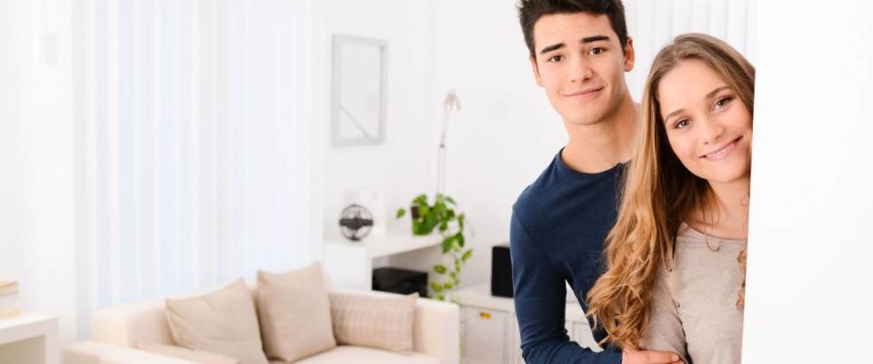 happy young couple opening door and welcoming their friends in apartment