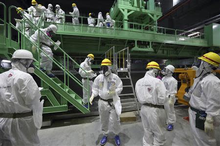 Members of the media and Tokyo Electric Power Co. (TEPCO) employees wearing protective suits and masks walk down the steps of a fuel handling machine on the spent fuel pool inside the No.4 reactor building at TEPCO's tsunami-crippled Fukushima Daiichi nuclear power plant in Fukushima prefecture in this November 7, 2013 file photo. REUTERS/Tomohiro Ohsumi/Pool/Files