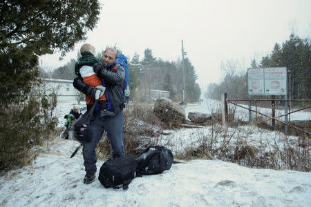 A man carries a child as a group that claimed to be from Syria crosses the U.S.-Canada border into Hemmingford, Quebec. REUTERS/Dario Ayala