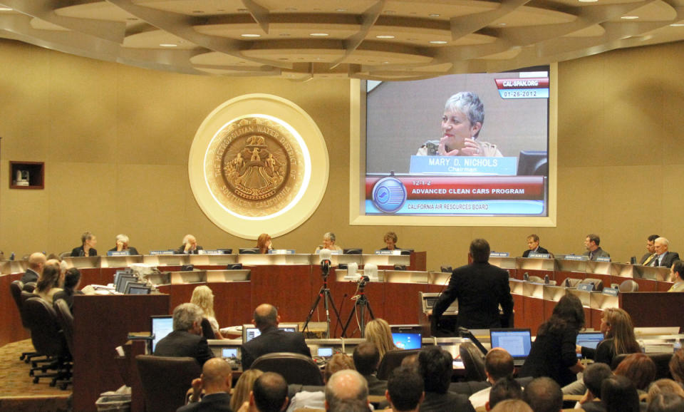 Mike Love of Toyota is at the podium at a meeting of the California Air Resources Board, with chair Mary D. Nichols projected on the screen, in Los Angeles, Jan. 26, 2012, before a vote on new rules that would require automakers to build cars and trucks by 2025 that emit about three-quarters less smog producing pollutants, and also mandate that one of every seven new cars sold in the state be a zero emission or plug-in hybrid vehicle.