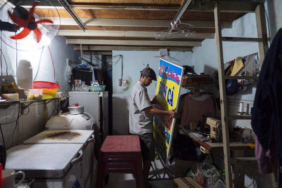 Pham Van Sang, a street food vendor who moved from the Mekong Delta for a better life, brings his business sign into his cluttered apartment after wrapping up for the day in Ho Chi Minh City, Vietnam, Monday, Jan. 22, 2024. Pham earns his living by selling noodles in the city's industrial zone, a destination for many migrants like himself from the Mekong Delta. (AP Photo/Jae C. Hong)