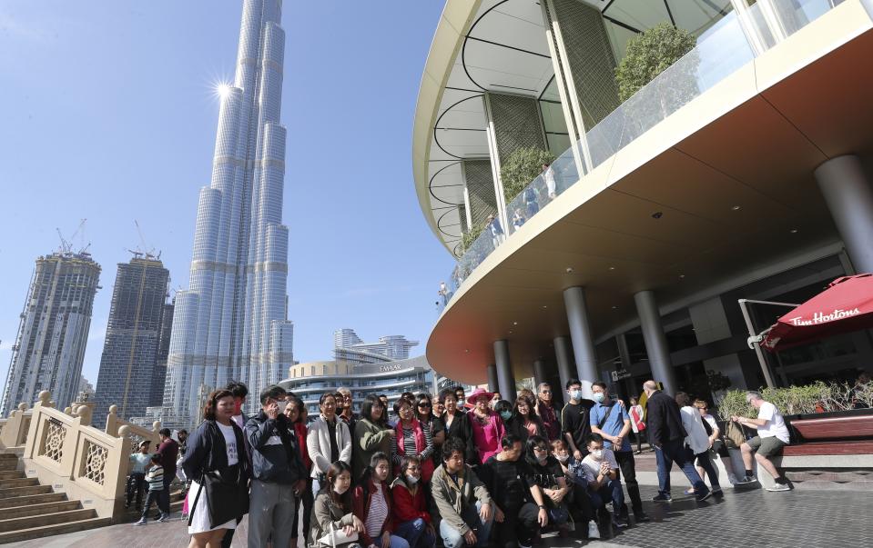 In this Thursday, Jan. 30, 2020, photo, a group of Chinese tourists some of them with face mask pose for a photo under the world's tallest tower, Burj Khalifa, in Dubai, United Arab Emirates. The World Health Organization declared the outbreak sparked by a new virus in China that has been exported to more than a dozen countries as a global emergency Thursday after the number of cases spiked tenfold in a week. (AP Photo/Kamran Jebreili)