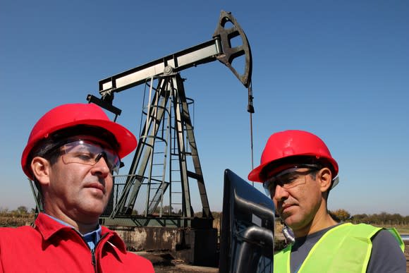 Oilfield workers next to a pump jack working with a laptop.