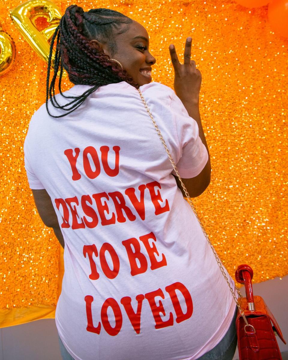 A woman with her back to the camera, revealing the message on the back of her T-shirt: "You deserve to be loved"
