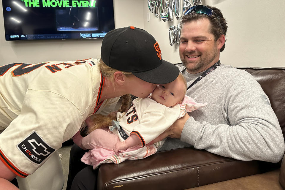 San Francisco Giants major league assistant coach Alyssa Nakken, left, kisses her daughter, Austyn, as her husband, Robert, watches before a baseball game between the Giants and the San Diego Padres in San Francisco, Friday, April 5, 2024. (AP Photo/Janie McCauley)