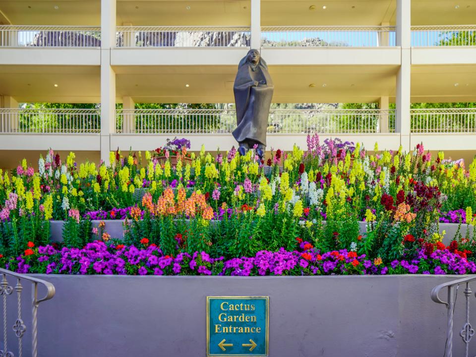 A statue on top of flowers with a sign that says "Cactus Garden Entrance" beneath it