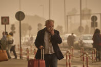 A passenger covers his nose and mouth in a cloud of red dust at the airport in Santa Cruz de Tenerife, Spain, Sunday, Feb. 23, 2020. Flights leaving Tenerife have been affected after storms of red sand from Africa's Saharan desert hit the Canary Islands. (AP Photo/Andres Gutierrez)
