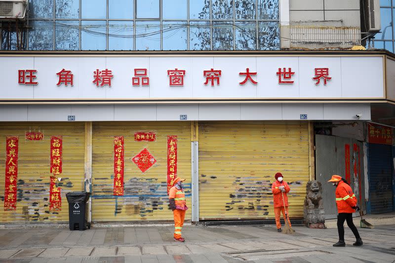 Cleaning workers wear face masks outside a closed shop following an outbreak of the novel coronavirus in Wuhan