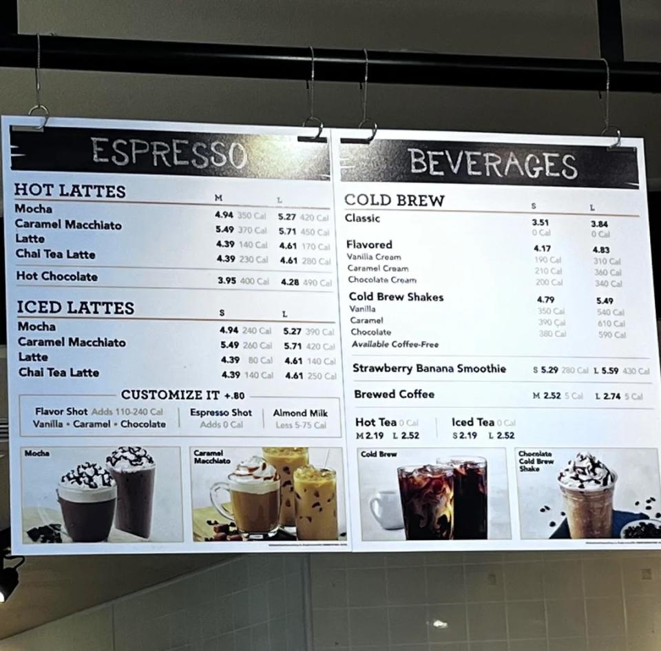 Menu board with a selection of hot lattes, iced lattes, cold drinks and tea options with prices in a cafe
