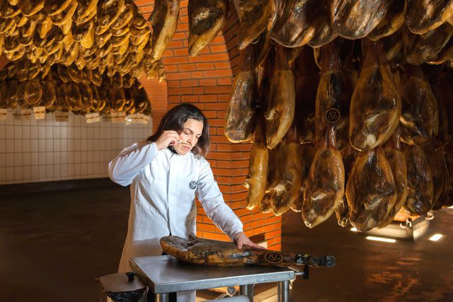 <p>Courtesy of 5J</p> Cristina Sánchez, the cellar master at 5J, in Jabugo, tests a leg of jamón ibérico.