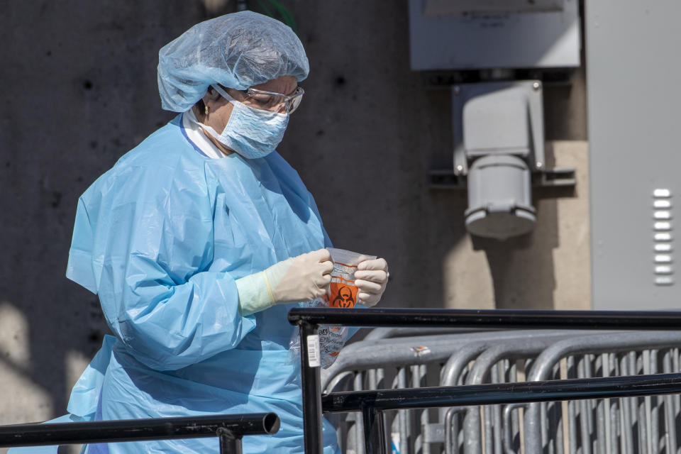 A member of the Brooklyn Hospital Center COVID-19 testing team holds a biohazard bag outside their testing site, Thursday, March 26, 2020, in New York. The new coronavirus causes mild or moderate symptoms for most people, but for some, especially older adults and people with existing health problems, it can cause more severe illness or death. (AP Photo/Mary Altaffer)