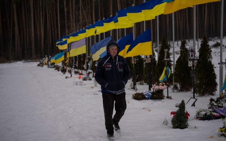 An undertaker walks by the Alley of Heroes at the Irpin Cemetery in Ukraine - Daniel Cole/AP
