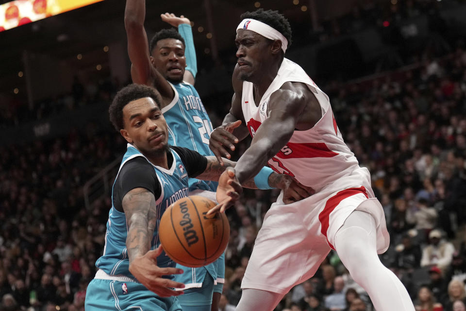 Toronto Raptors forward Pascal Siakam, right, passes the ball while under pressure from Charlotte Hornets forward P.J. Washington, bottom left, during second-half NBA basketball game action in Toronto, Monday, Dec. 18, 2023. (Nathan Denette/The Canadian Press via AP)