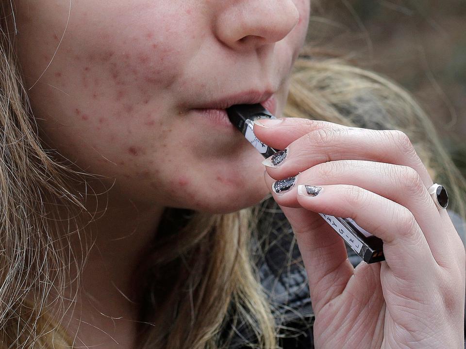 FILE - In this April 11, 2018, file photo, a high school student uses a vaping device near a school campus in Cambridge, Mass. U.S. health regulators are moving ahead with a plan to keep e-cigarettes out of the hands of teenagers by restricting sales of most flavored products in convenience stores and online. (AP Photo/Steven Senne, File)