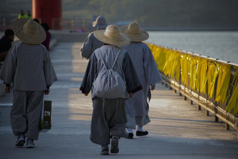 Monks walk past a railing lined with yellow ribbons symbolising hope for a safe return for missing passengers the 'Sewol' ferry at Jindo harbour on April 24, 2014