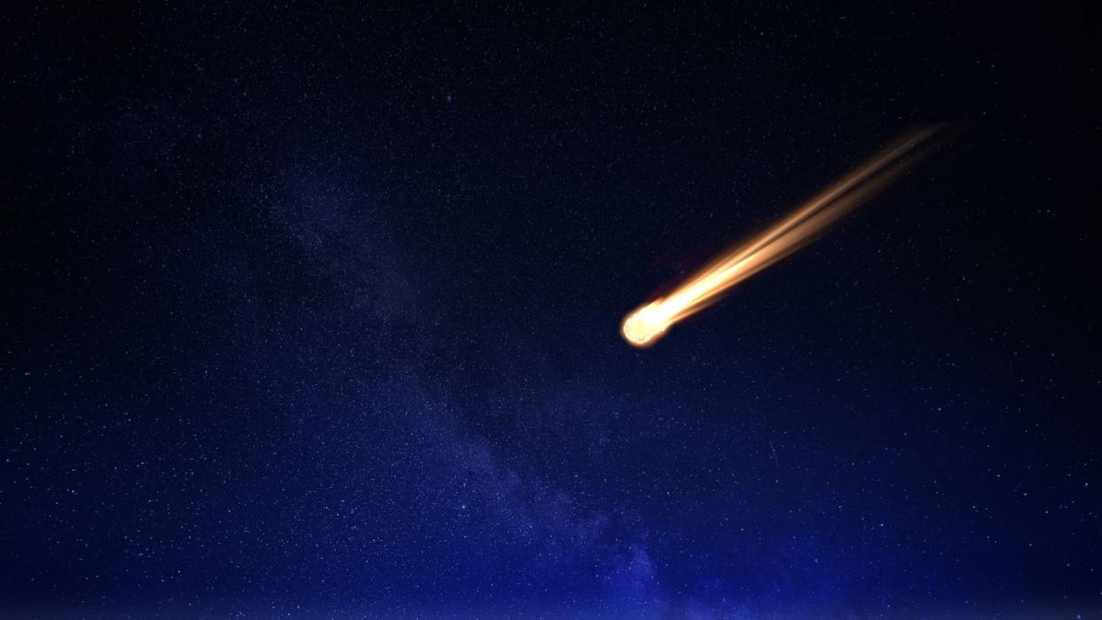 meteor in night sky falling over ocean
