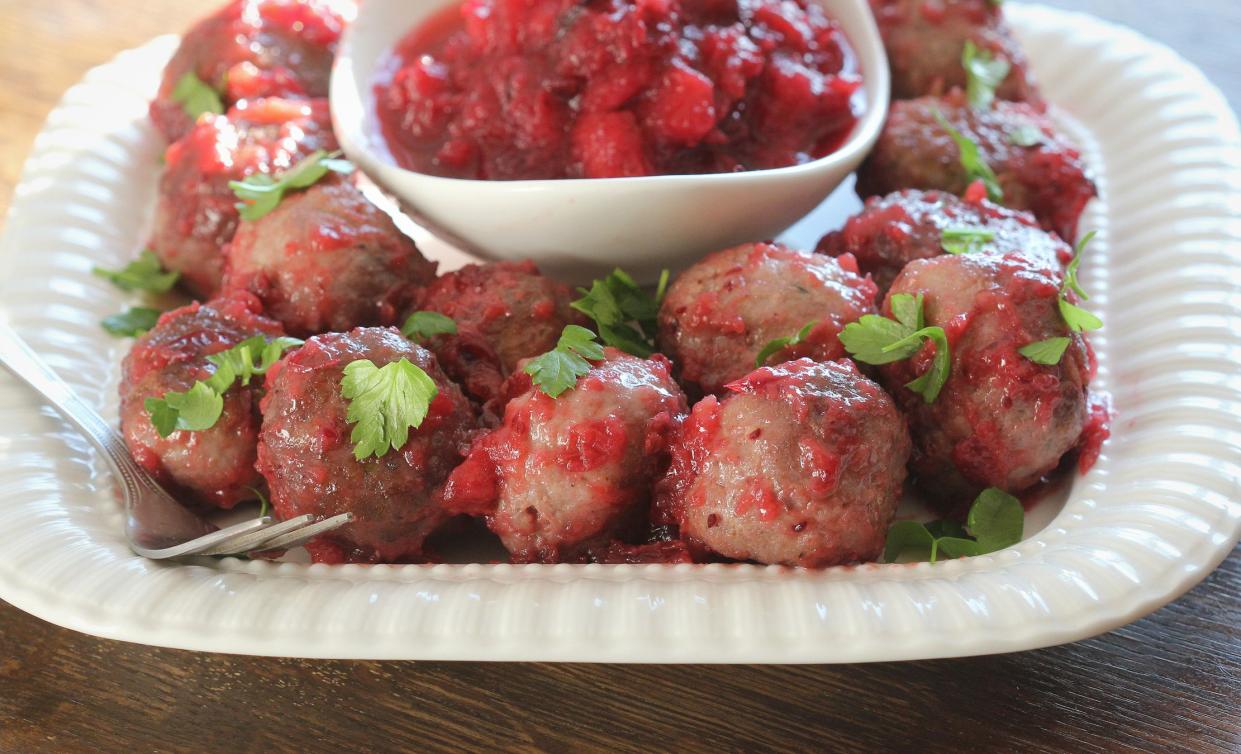 Hot meatballs with cranberry sauce on white plate .