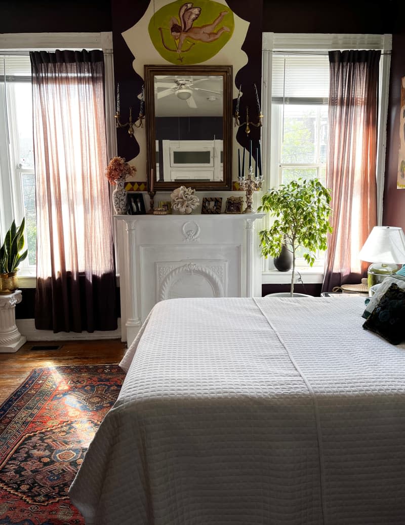 Mirror hangs above white mantel in eggplant bedroom with white bedding.