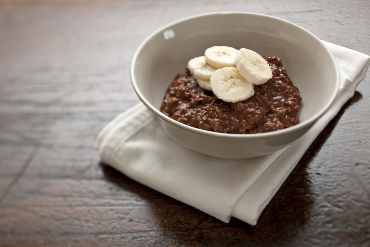 A white bowl of banana Nutella oatmeal on a white napkin on a rustic and worn dark wooden table