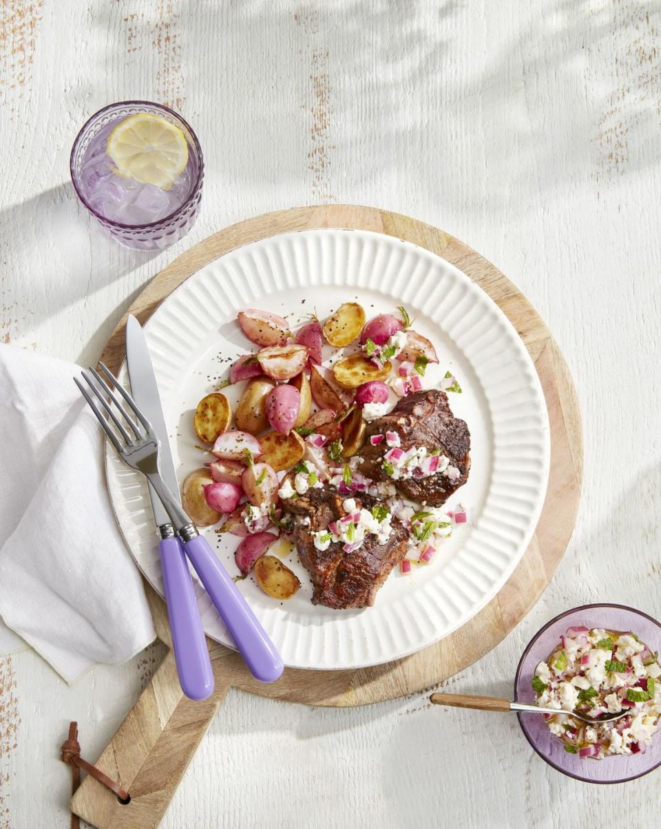 lamb chops with roasted potatoes and radishes on a white plate with a fork and knife