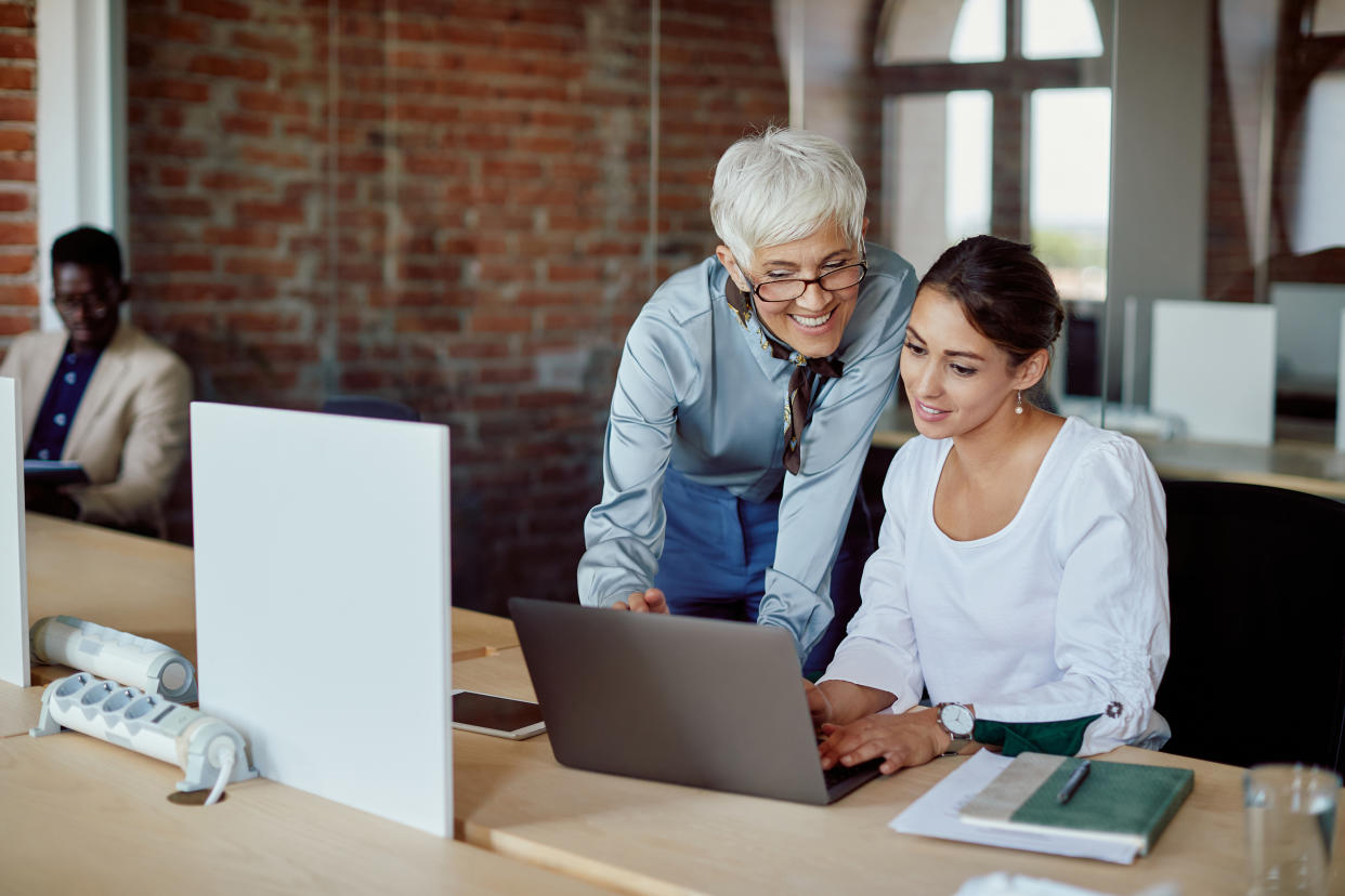 Happy mature executive assisting her younger coworker who is working on a computer in the office.