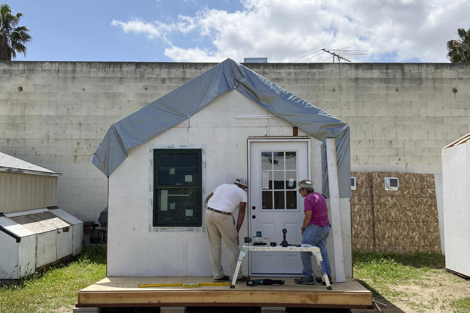 In this photo provided by Amikas, community volunteers install a steel door on cabin six at Meridian Baptist Church in El Cajon, Calif., on April 16, 2022. The sense of safety and security provided by the locking door is vital for the future occupants of the cabins. The Emergency Sleeping Cabins will serve as bridge housing for homeless single mothers with children. (Lisa Kogan/Amikas via AP)