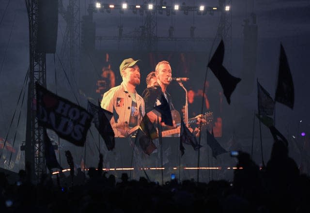 Members of Coldplay seen on a big screen surrounded by flags 