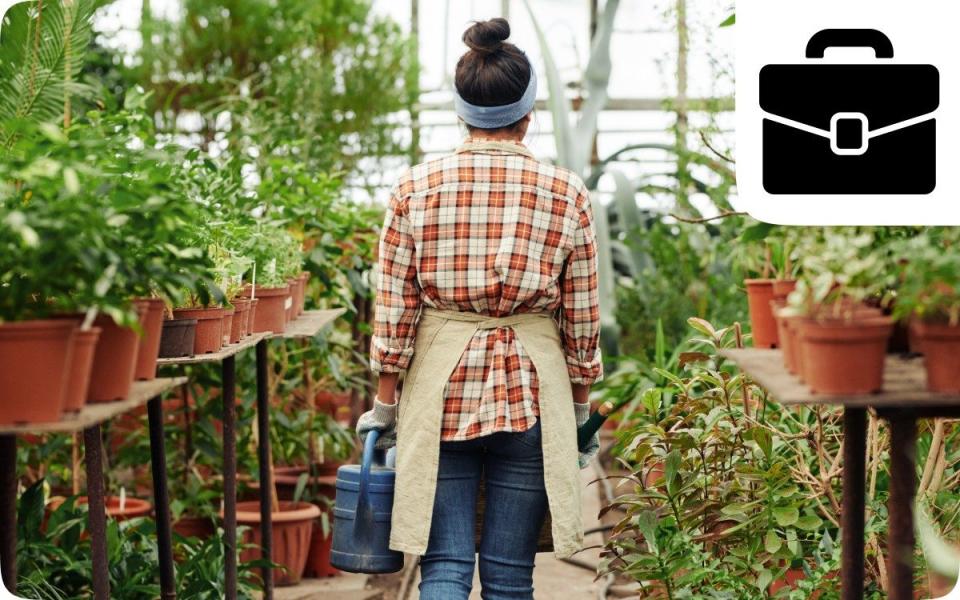 Woman gardener in a potting shed walks away with her back to the camera carrying a watering can