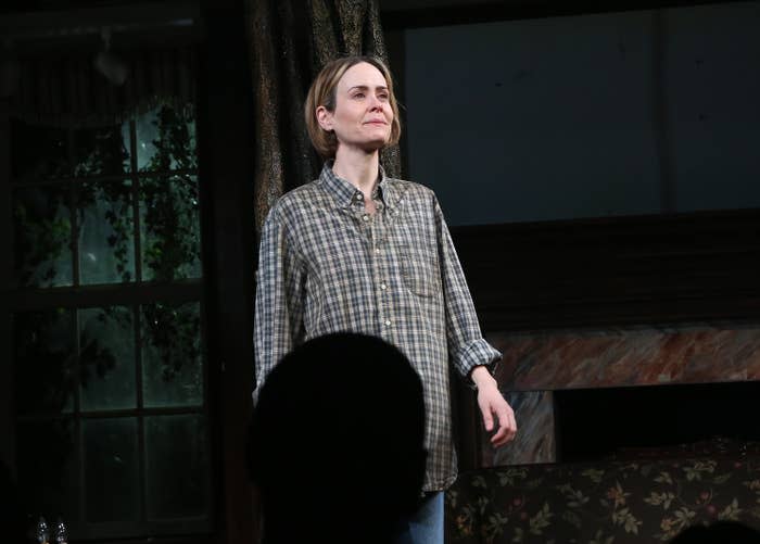 Sarah on stage in a plaid shirt and casual attire with a set resembling a living room