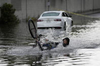 A cyclist falls while trying to ride through floodwaters near a stranded car, Friday, Sept. 1, 2023, in Las Vegas. (AP Photo/John Locher)