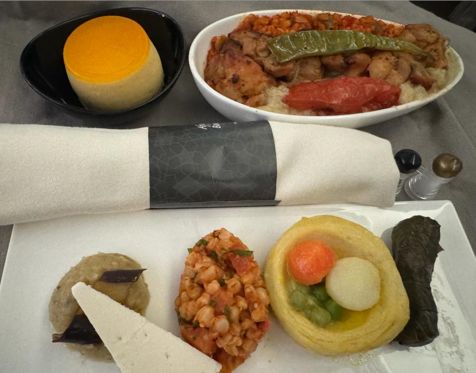 A selection of meze items on a plate, next to a dish of chicken, bulgar, tomato, and peppers and a tart in a bowl.