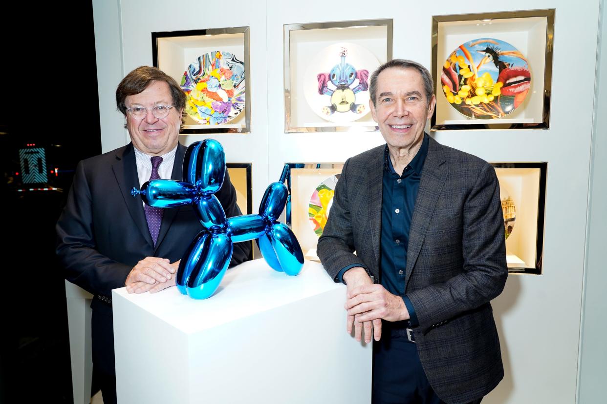 Jeff Koons and Michel Bernardaud stand next to Koons' blue balloon dog sculpture, a shiny blue piece that looks like a balloon animal fashioned into the shape of a dog.