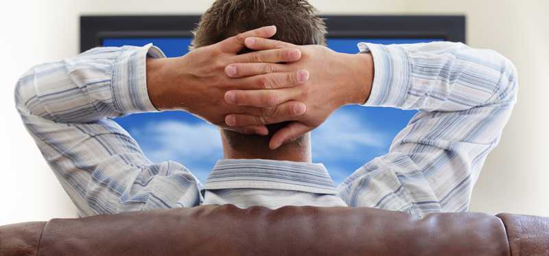 Man watching tv with hands rested behind his head.