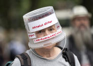 A demonstrator walks through Berlin-Charlottenburg with a plastic bucket placed on his head reading 'Absolutely safe against the stupidity virus', in Berlin, Sunday Aug. 1, 2021, during a protest against coronavirus restrictions. Hundreds have turned out in Berlin to protest the German government’s anti-coronavirus measures despite a ban on the gatherings, leading to arrests and clashes with police. (Fabian Sommer/dpa via AP)