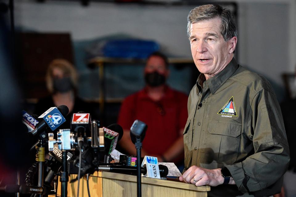 North Carolina Governor Roy Cooper stands in front of a row of muddied volunteers as he speaks to the press at BearWaters Brewing in Canton August 19, 2021, shortly fatal floods hit the region.