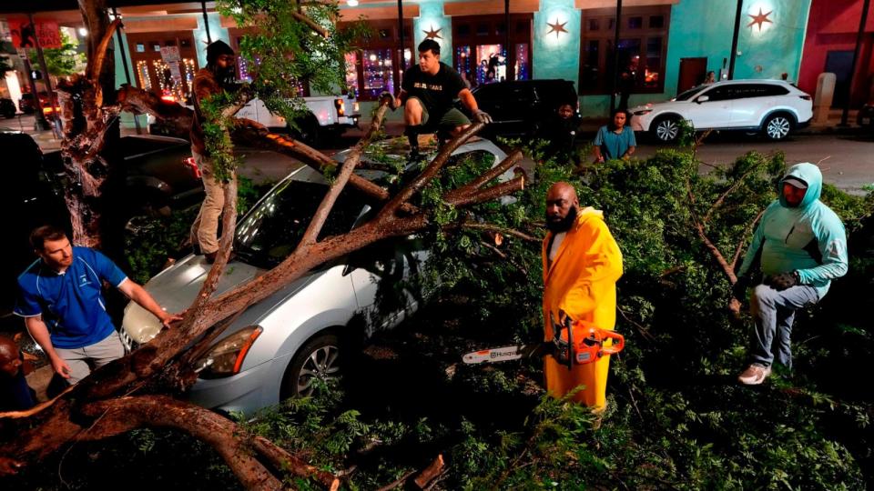 PHOTO: Rapper Trae tha Truth, in yellow, cuts fallen tree limbs on top of a car in the aftermath of a severe thunderstorm that passed through downtown,  May 16, 2024, in Houston.  (David J. Phillip/AP)