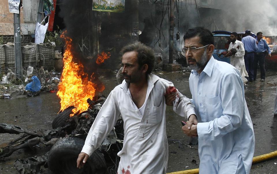 A man helps an injured man walk away from the site of a bomb attack in Peshawar September 29, 2013. Twin blasts in the northwestern Pakistan city of Peshawar killed 33 people and wounded 70 on Sunday, a week after two bombings at a church in the frontier city killed scores, police and hospital authorities said.REUTERS/Khuram Parvez (PAKISTAN - Tags: CIVIL UNREST CRIME LAW POLITICS)