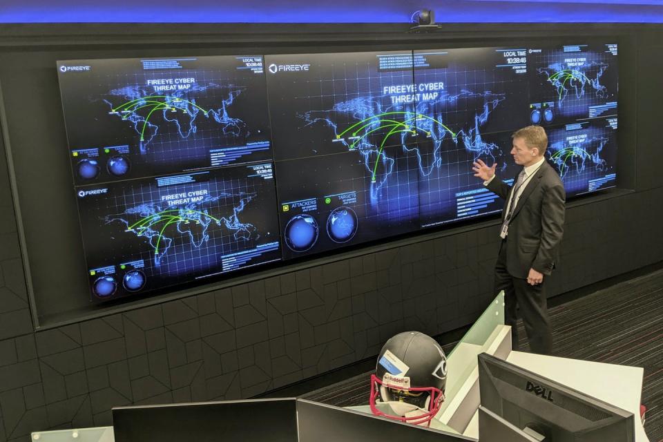 A man stands in front of a wall covered with computer displays showing maps of the world