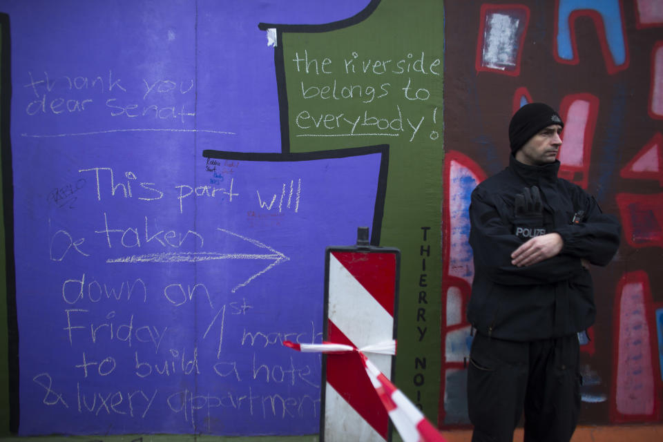 A German police officer protects a part of the former Berlin Wall in Berlin, Germany, Friday, March 1, 2013. Construction crews stopped work Friday on removing a small section from one of the few remaining stretches of the Berlin Wall to make way for a condo project after hundreds of protesters blocked their path.(AP Photo/Markus Schreiber)