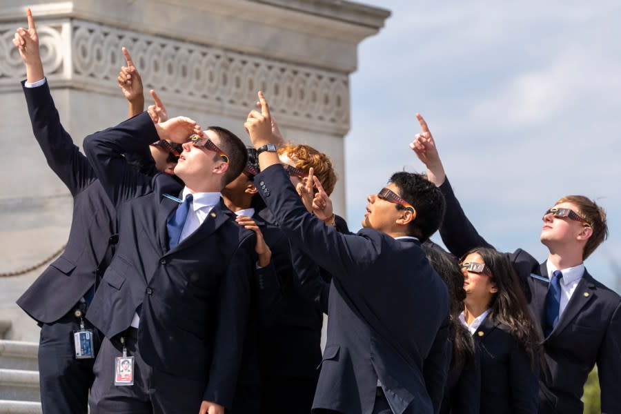 Senate pages wear eclipse glasses as they view the moon partially covering the sun during a total solar eclipse, in front of the U.S. Senate on Capitol Hill, Monday, April 8, 2024, in Washington. (AP Photo/Alex Brandon)