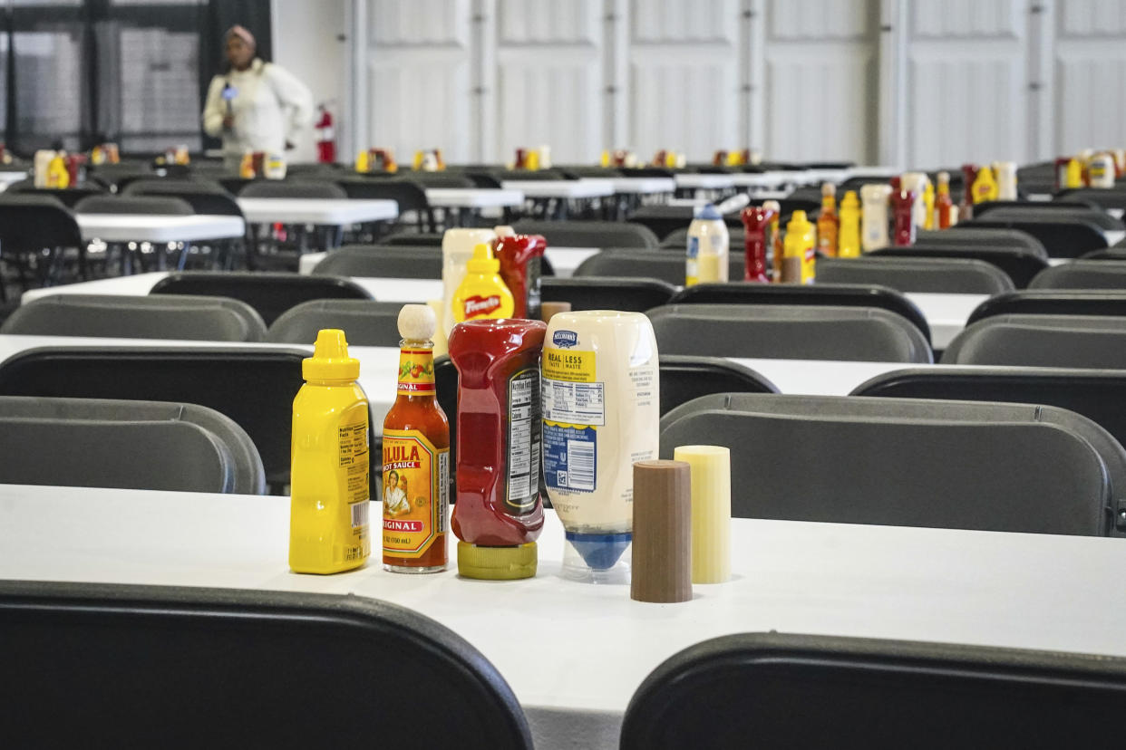 Tables set with condiments for scores of individuals, shown during a media tour, is part of New York City's latest temporary shelter on Randall's Island for migrants being bused into the city by southern border states, Oct. 18, 2022, in New York. The shelter will start taking in single adult men on Wednesday, Oct. 19, with facilities including laundry, a mass sleeping area, entertainment and recreation. (AP Photo/Bebeto Matthews)