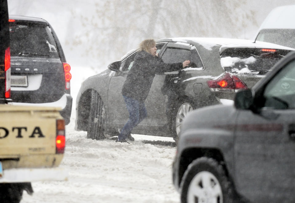 A woman tries to push a stuck car in the snow at the intersection of State Street and Divide Avenue in Bismarck, N.D., Tuesday, April 12, 2022. (Mike McCleary/The Bismarck Tribune via AP)