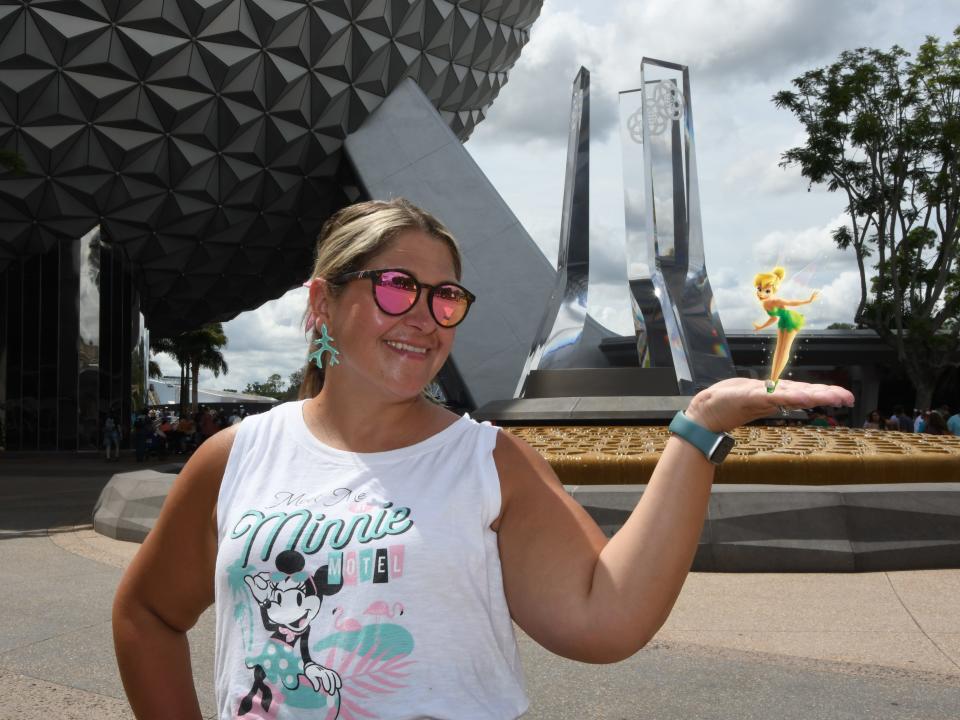 terri posing in front of the epcot ball with tinkerbell superimposed into her hand