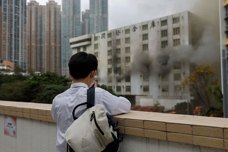 A person looks at a blaze at a warehouse in the city's bustling Kowloon district