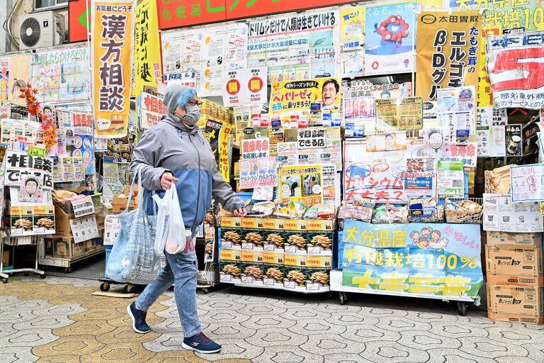 Esta foto tomada el 15 de marzo de 2024 muestra a una mujer pasando por una tienda cubierta de publicidad a lo largo de una calle comercial en el centro de Osaka.